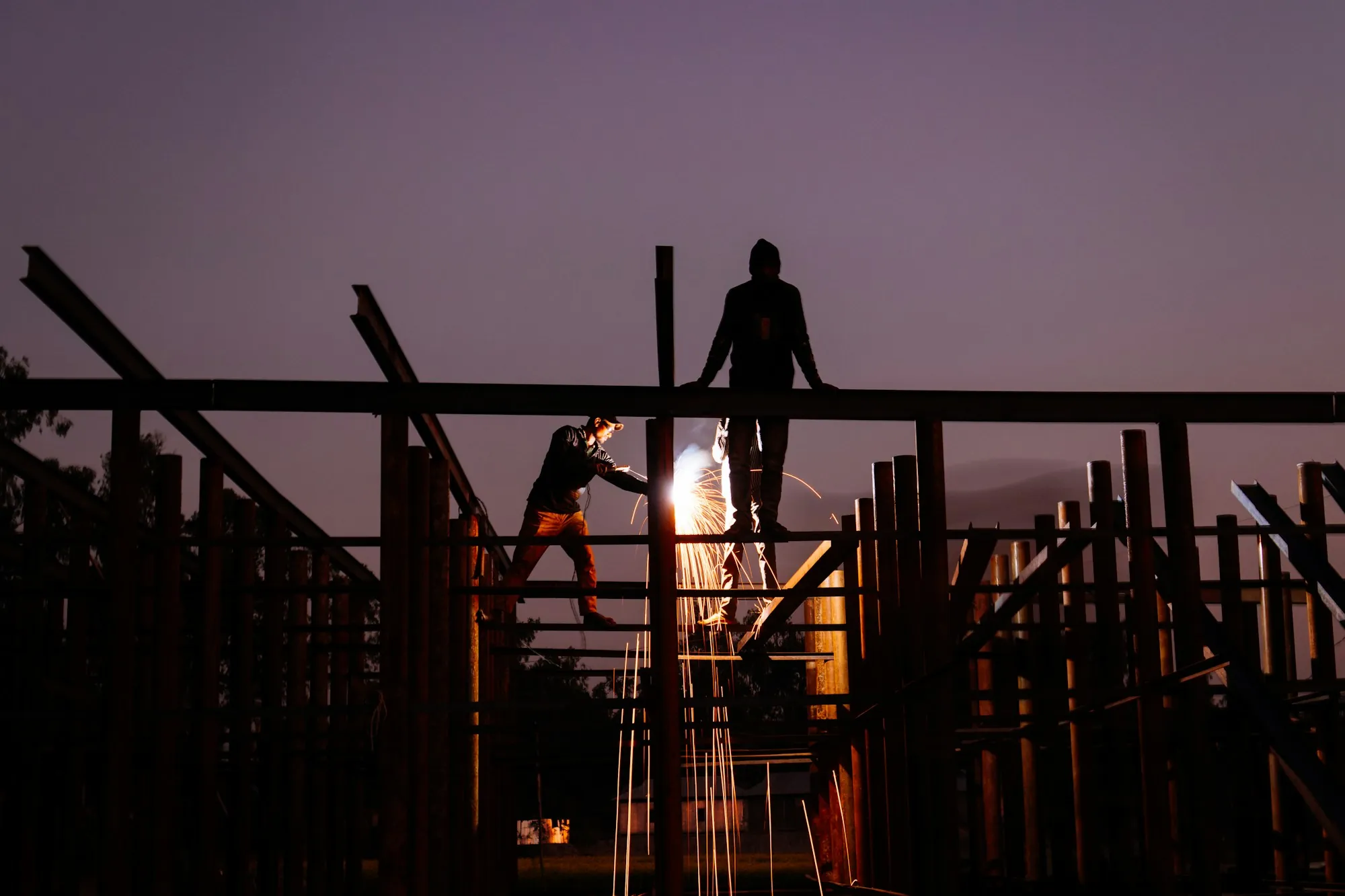 Silhouettes of workers on roof framing at dusk