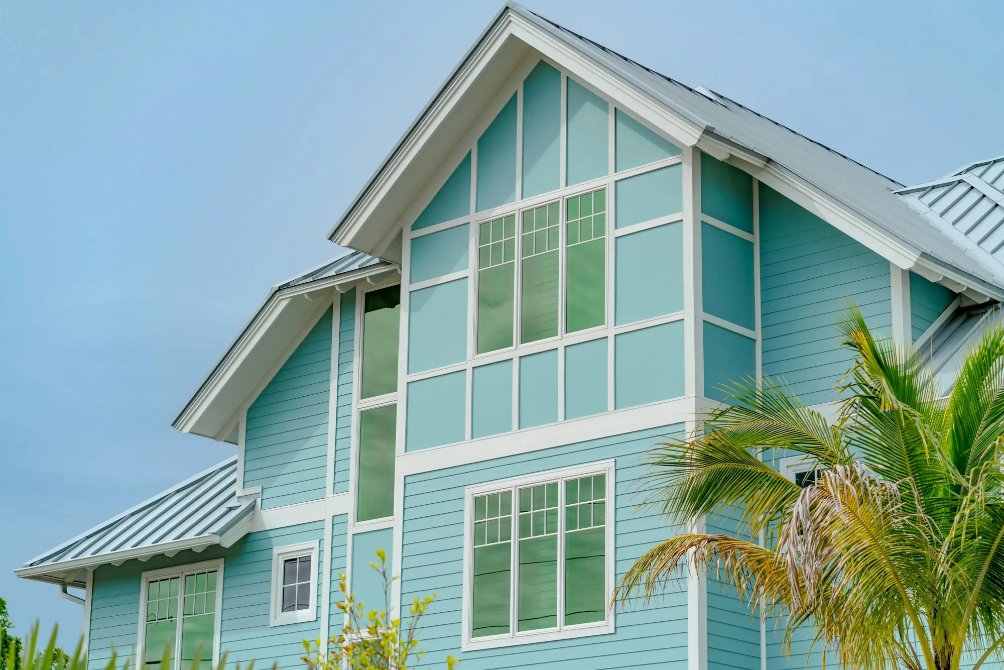 Teal coastal house with a metal roof and tall windows