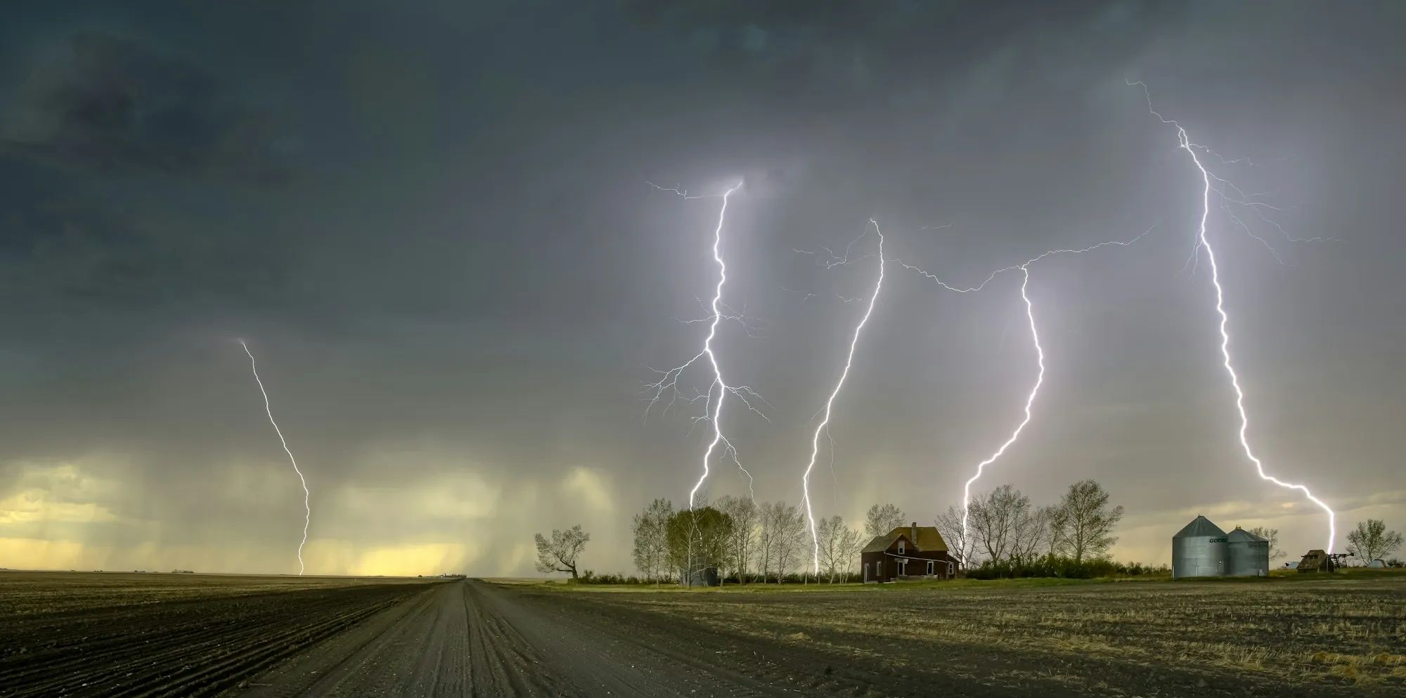 Multiple lightning strikes over a rural road and farmhouse