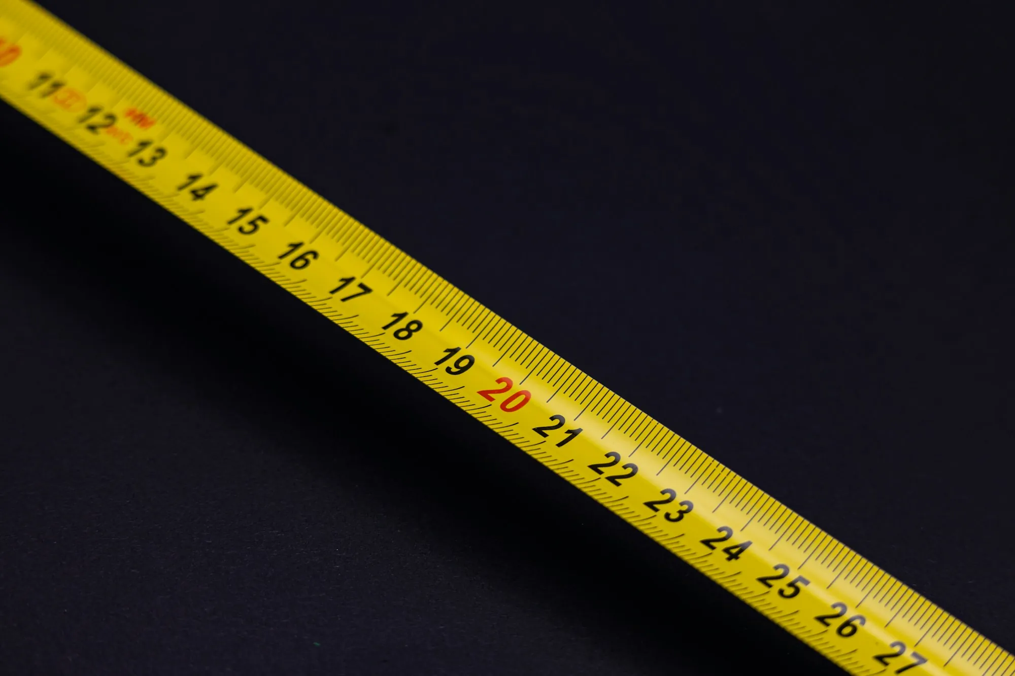 Yellow tape measure blade stretched diagonally on a dark surface